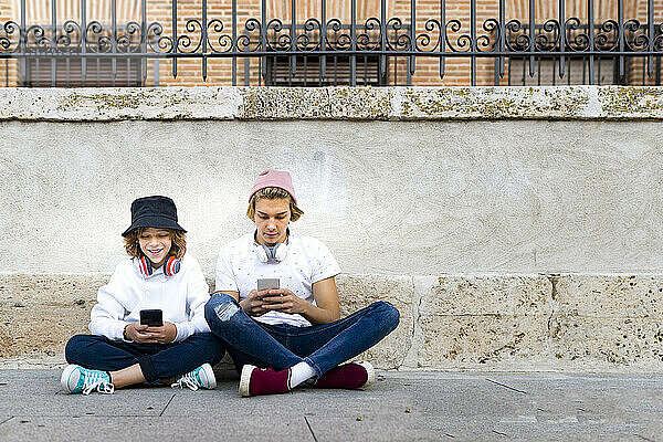 Freunde mit Strickmütze benutzen Mobiltelefone  während sie auf dem Gehweg sitzen