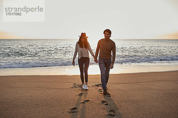 Paar hält sich beim Spazierengehen am Strand an den Händen
