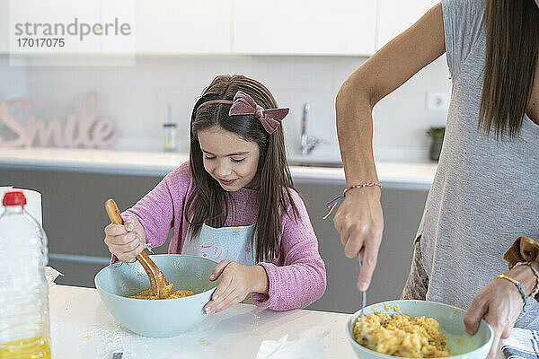 Tochter bereitet Muffin zu und steht neben ihrer Mutter in der Küche