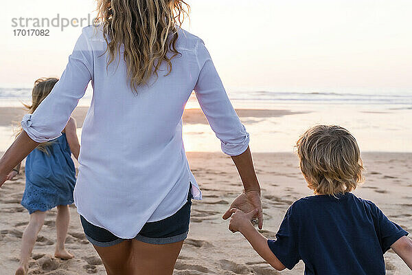 Mutter mit Kindern läuft bei Sonnenuntergang zum Meer