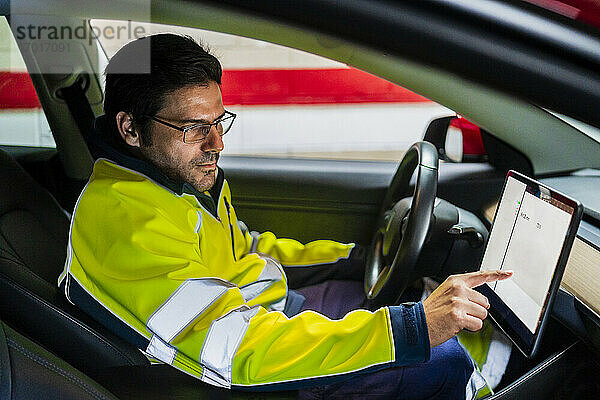 Männlicher Techniker in Uniform programmiert auf einem digitalen Tablet im Auto