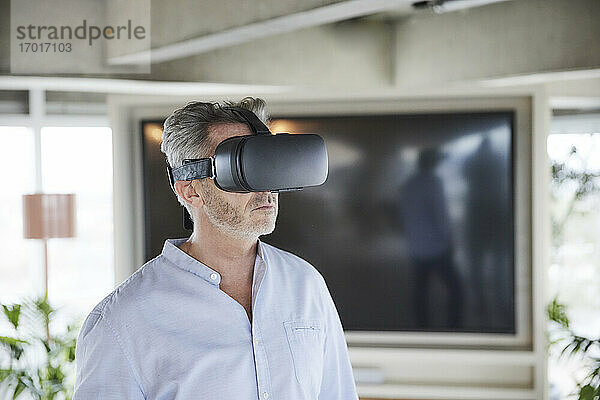 Älterer Geschäftsmann  der ein Virtual-Reality-Headset benutzt  während er zu Hause steht