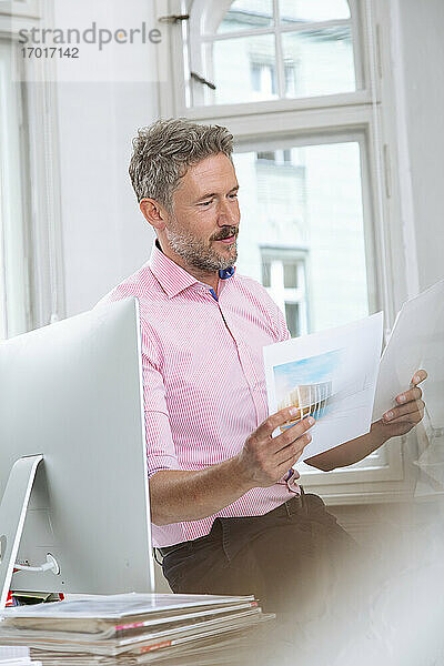 Älterer Geschäftsmann  der am Computer in einer Bürokabine ein Dokument liest