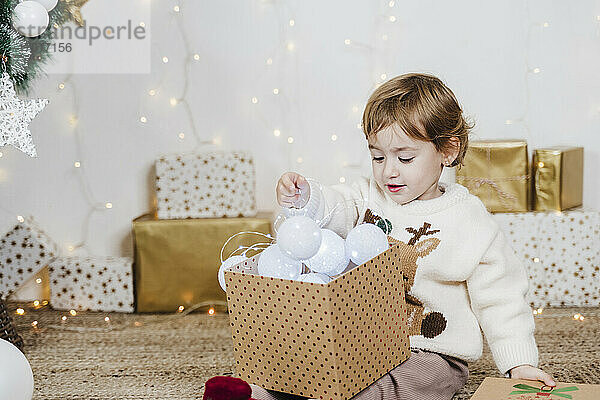Baby-Mädchen hält Weihnachtsbeleuchtung in Geschenk-Box  während zu Hause sitzen