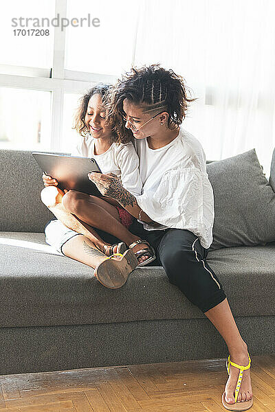 Mutter und Tochter sitzen zusammen auf dem Sofa mit digitalem Tablet