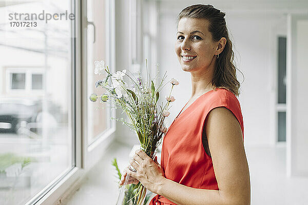 Porträt einer lächelnden Frau mit Blumen am Fenster