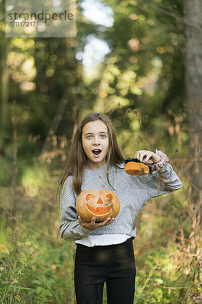 Mädchen mit offenem Mund steht mit Halloween-Kürbis im Park