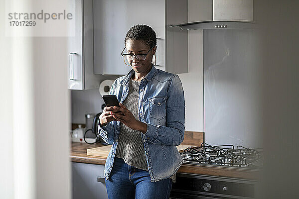 Frau schaut in der Küche auf ihr Smartphone