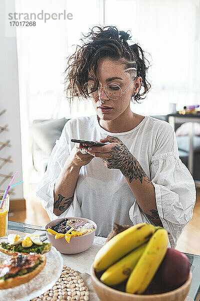 Porträt einer jungen Frau  die beim Frühstück mit ihrem Smartphone spielt