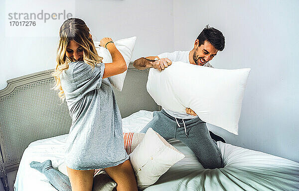 Glückliches junges Paar mit einer Kissenschlacht im Bett zu Hause