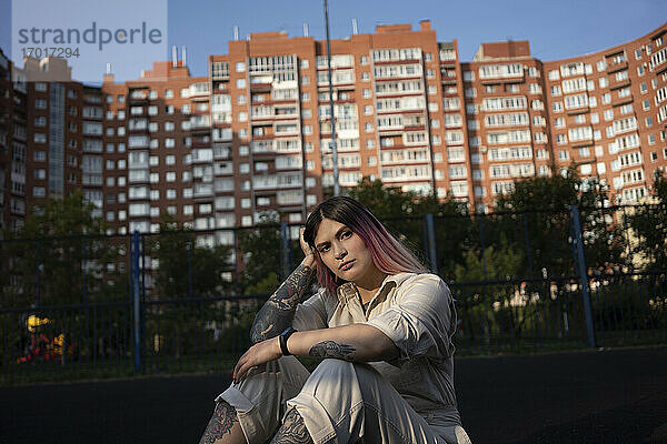 Junge Frau mit Hand im Haar auf einem Sportplatz vor einem Gebäude