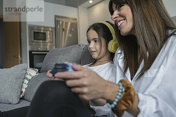 Glückliche Mutter und Tochter spielen zusammen Videospiele im Wohnzimmer