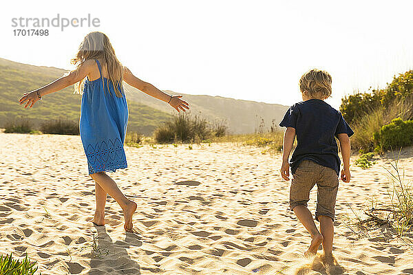 Bruder und Schwester spielen  während sie auf Sand laufen