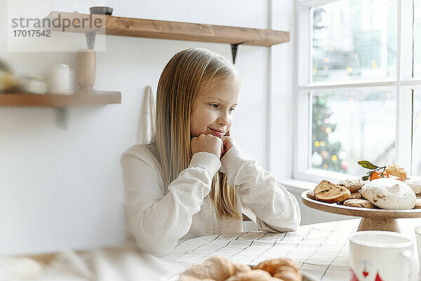 Lächelndes Mädchen betrachtet Kekse auf dem Tisch in der Küche