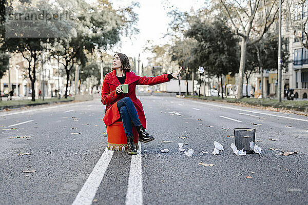 Junge Frau in Winterjacke mit Kaffeetasse wirft zerknülltes Papier aus dem Mülleimer auf die Straße