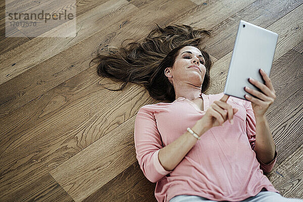 Reife Frau  die ein digitales Tablet benutzt  während sie in einer Wohnung auf dem Boden liegt