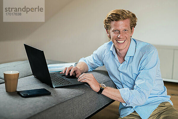 Lächelnder Geschäftsmann mit Laptop auf der Couch zu Hause