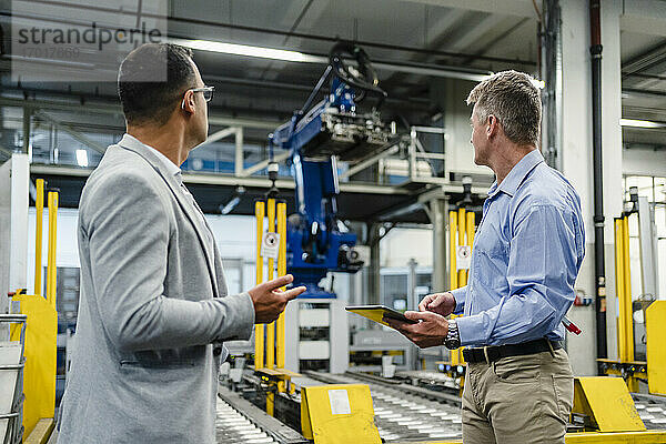 Männliche Fachkräfte mit digitalem Tablet  die sich die Maschinenausstattung in einer Fabrik ansehen
