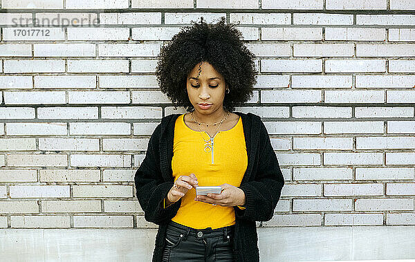 Schöne Frau mit Afro-Haar  die ein Smartphone benutzt  während sie an einer Mauer steht