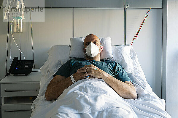 Patient mit Gesichtsschutzmaske auf dem Bett im Krankenhaus liegend