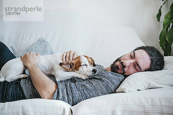 Mann schläft mit Hund auf dem Sofa zu Hause