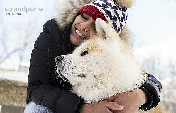 Glückliche Frau mit geschlossenen Augen umarmt Hund im Winter