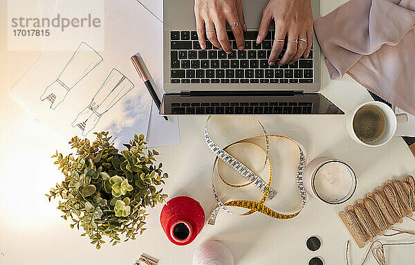 Modedesigner mit Laptop  Stoffmustern und Kaffee am Schreibtisch im Atelier
