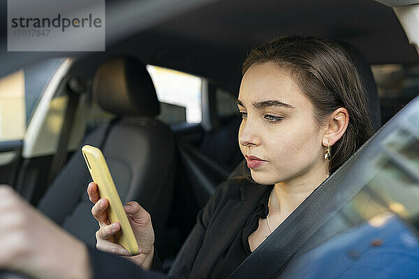 Geschäftsfrau  die im Auto sitzend ein Mobiltelefon benutzt