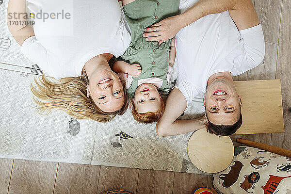 Porträt einer glücklichen Familie mit einer kleinen Tochter  die zu Hause auf dem Boden liegt