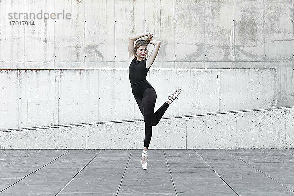 Ballerina im schwarzen Trikot tanzt vor einer Betonwand