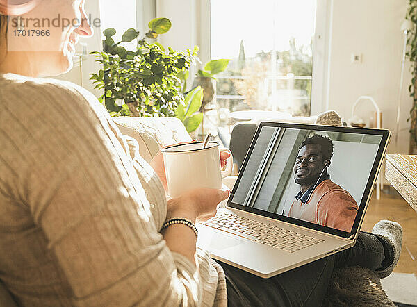 Junger Mann lächelt während eines Videogesprächs mit einer Frau auf dem Laptop-Bildschirm