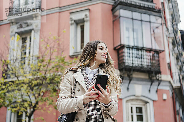Frau schaut weg  während sie ihr Handy gegen ein Gebäude in der Stadt hält