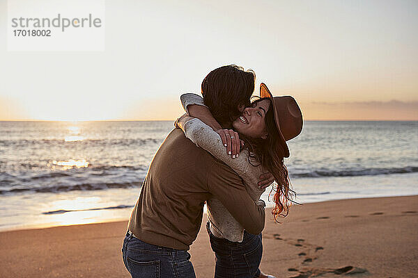 Junges Paar umarmt sich am Strand stehend