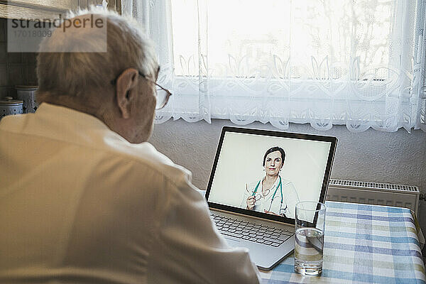 Älterer Mann lässt sich von einer Ärztin per Videoanruf auf dem Laptop zu Hause beraten