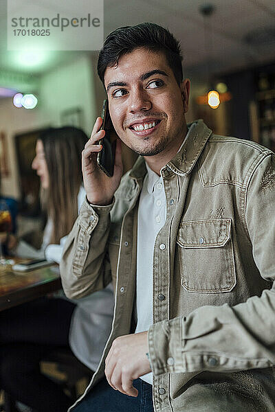 Lächelnder Mann  der in einer Bar mit dem Handy telefoniert und dabei wegschaut