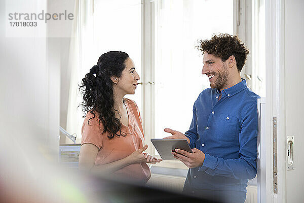 Glückliche männliche Fachkraft im Gespräch mit einer weiblichen Kollegin  die ein digitales Tablet in einer Bürobesprechung hält