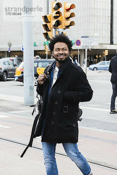 Lächelnder Mann mit Afro-Haar  der beim Gehen auf der Straße in der Stadt wegschaut