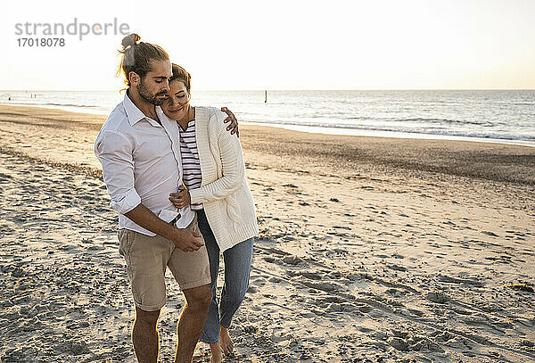 Romantisches junges Paar  das an einem sonnigen Tag am Strand spazieren geht