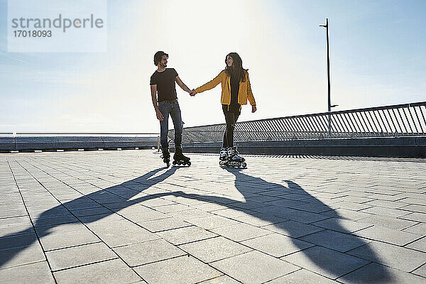 Junges Paar  das sich beim Rollschuhlaufen auf dem Pier an einem sonnigen Tag ansieht