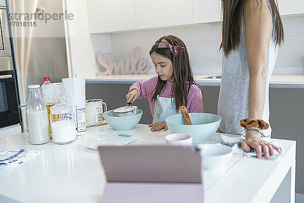 Tochter bereitet Muffin zu  während die Mutter in der Küche steht