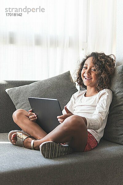 Porträt eines kleinen Mädchens lächelnd auf dem Sofa mit digitalem Tablet in den Händen