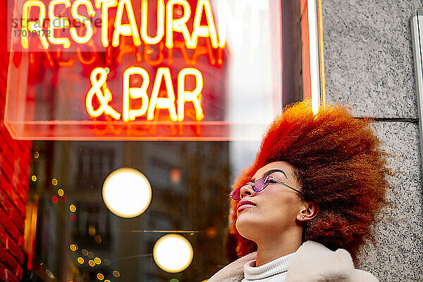 Stilvolle Frau mit Afro-Haar und Sonnenbrille vor einem Restaurant