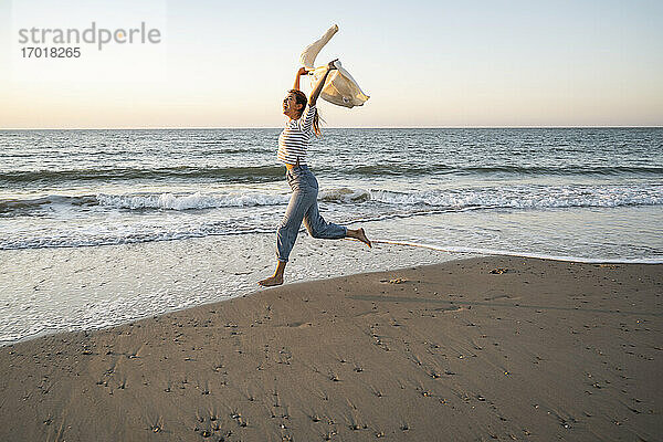 Sorglose Frau läuft am Strand gegen den klaren Himmel bei Sonnenuntergang