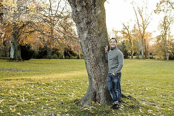 Lächelnder Mann an einem Baumstamm in einem öffentlichen Park im Herbst