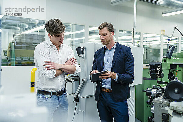 Geschäftsmann diskutiert mit einem männlichen Mitarbeiter über ein digitales Tablet in einer Fabrik