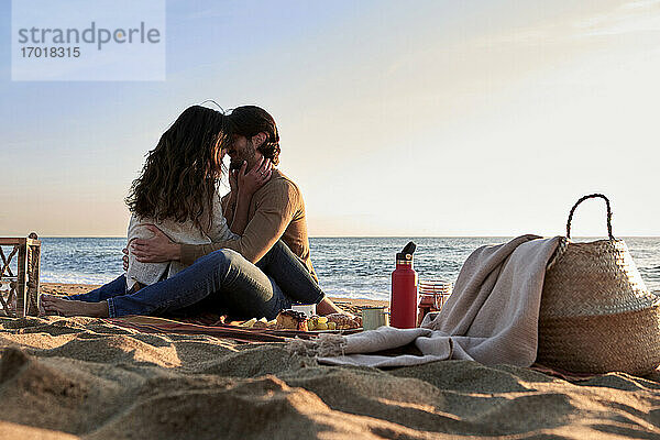 Freundin und Freund turtelnd von Angesicht zu Angesicht am Strand sitzend
