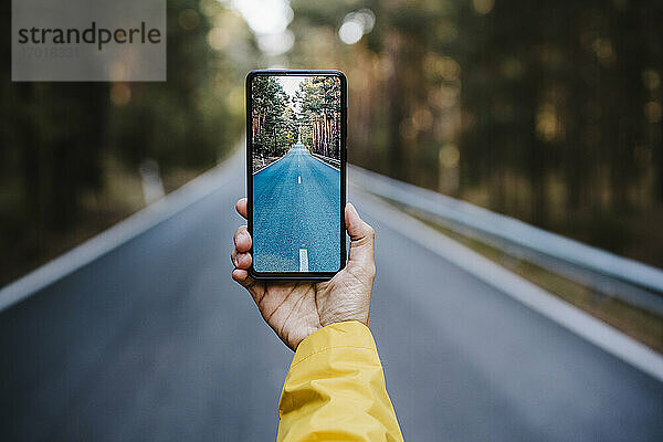 Eine Frau hält ihr Smartphone in der Hand und fotografiert eine leere Landstraße