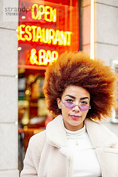 Schöne Frau mit Afro-Haar trägt eine Sonnenbrille und steht vor einem Restaurant