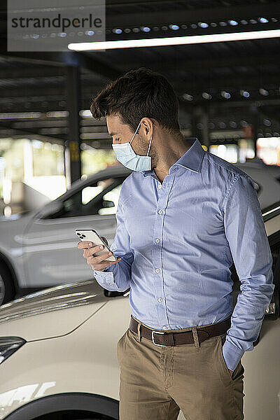 Geschäftsmann hält Smartphone auf einem Parkplatz während COVID-19