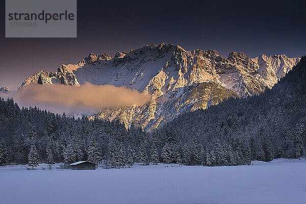 Landschaftlicher Blick auf verschneite Wälder und Berge bei Sonnenuntergang